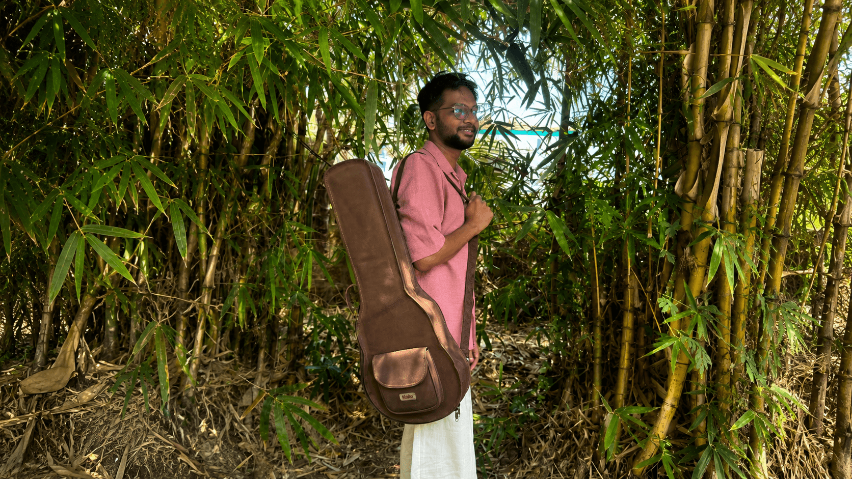 A musician in a bamboo grove carrying a brown leather Kailo instrument bag